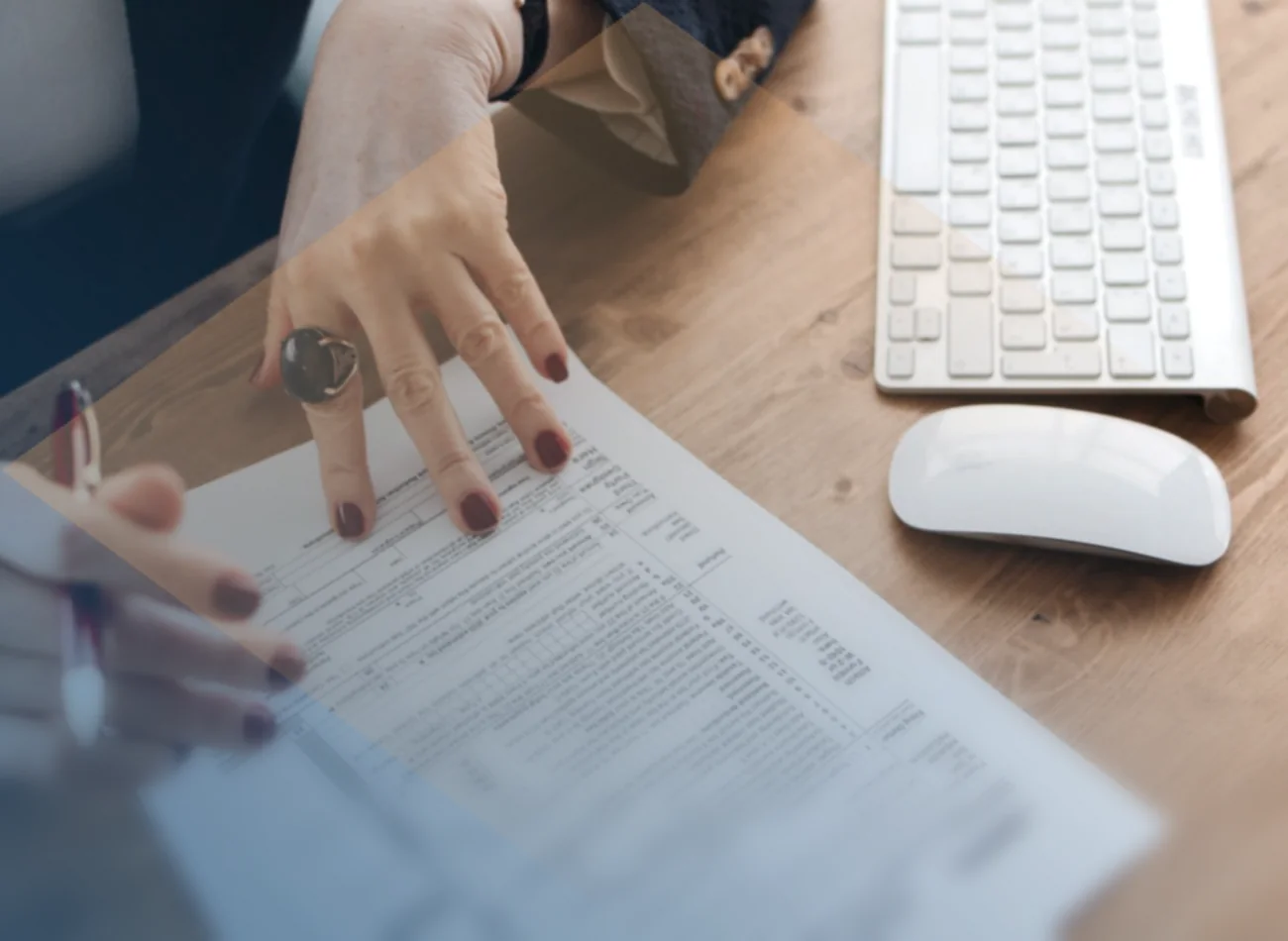 Hands settling paperwork at a desk beside a keyboard.